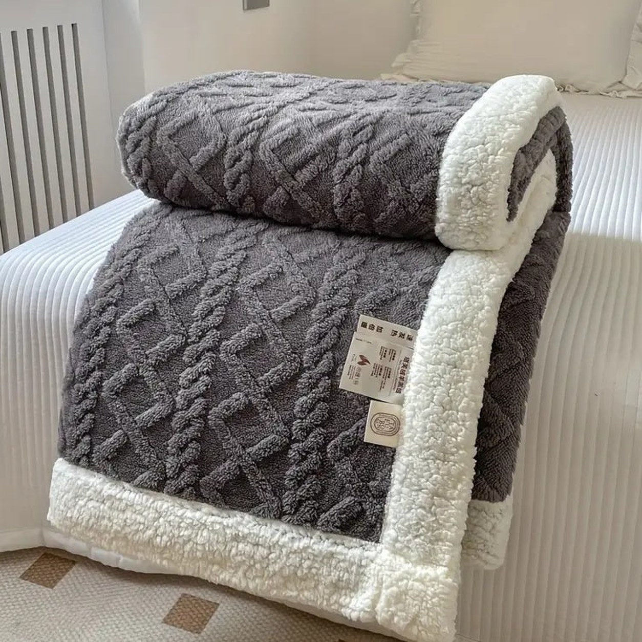 Gray sherpa throw blanket folded on a bed, the raised cable and diamond texture facing out