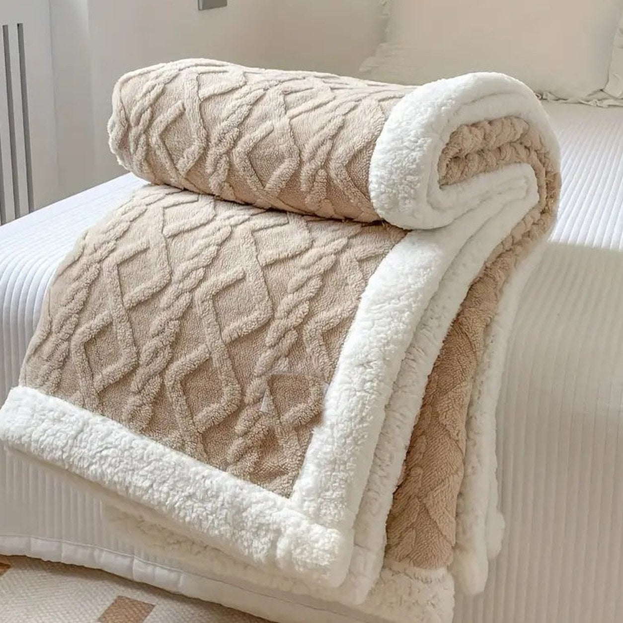 Taupe sherpa throw blanket folded on a bed, the raised cable texture facing out and the white sherpa lining showing at the fold