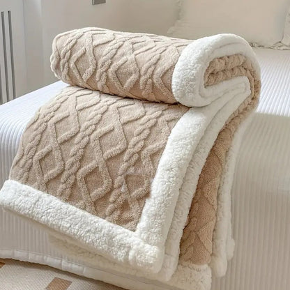 Taupe sherpa throw blanket folded on a bed, the raised cable texture facing out and the white sherpa lining showing at the fold