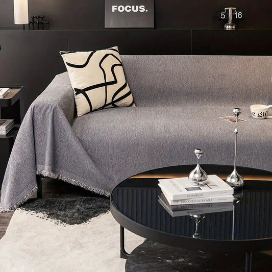 A gray chenille cover over a couch in a dark-walled living room, with the fringed edge hanging toward the floor.