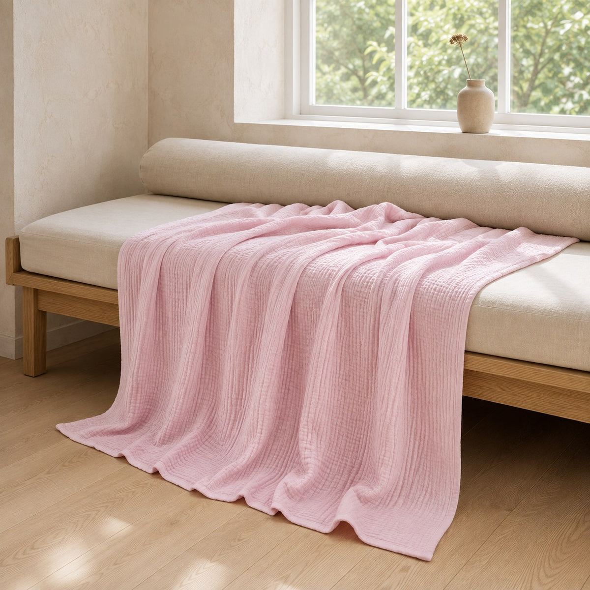 Pink muslin cotton blanket across an oak daybed under a window, falling in soft folds to the floor