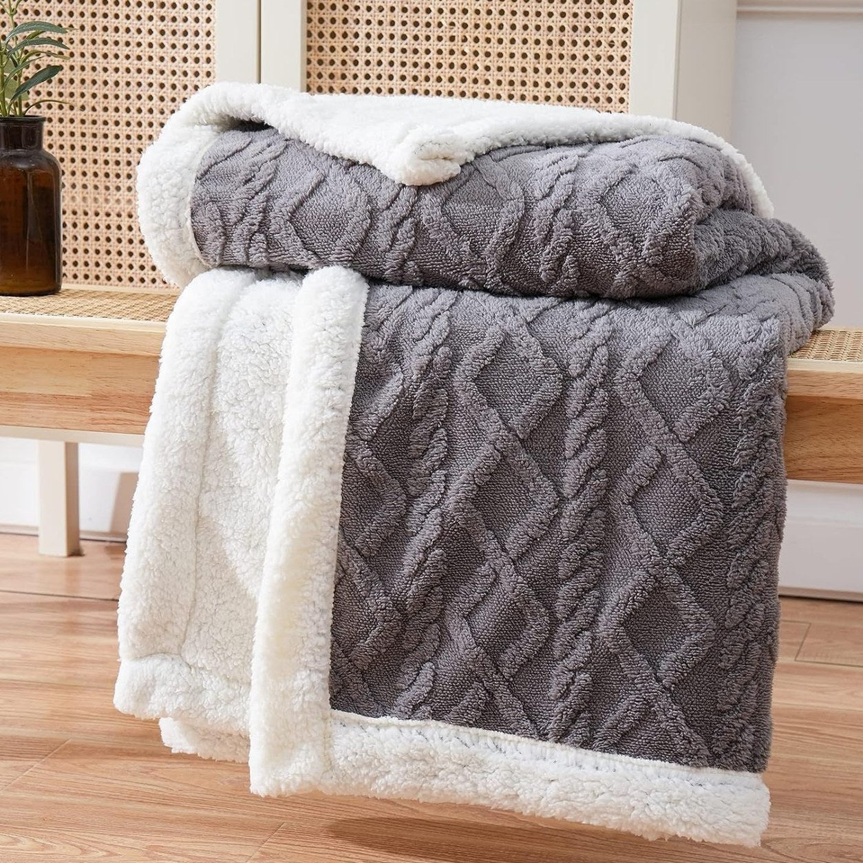 The gray sherpa throw blanket folded over a bench under a window