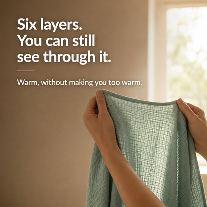 Hands holding the sage blanket up to a window with daylight coming through the open weave. Text reads: Six layers. You can still see through it. Warm, without making you too warm