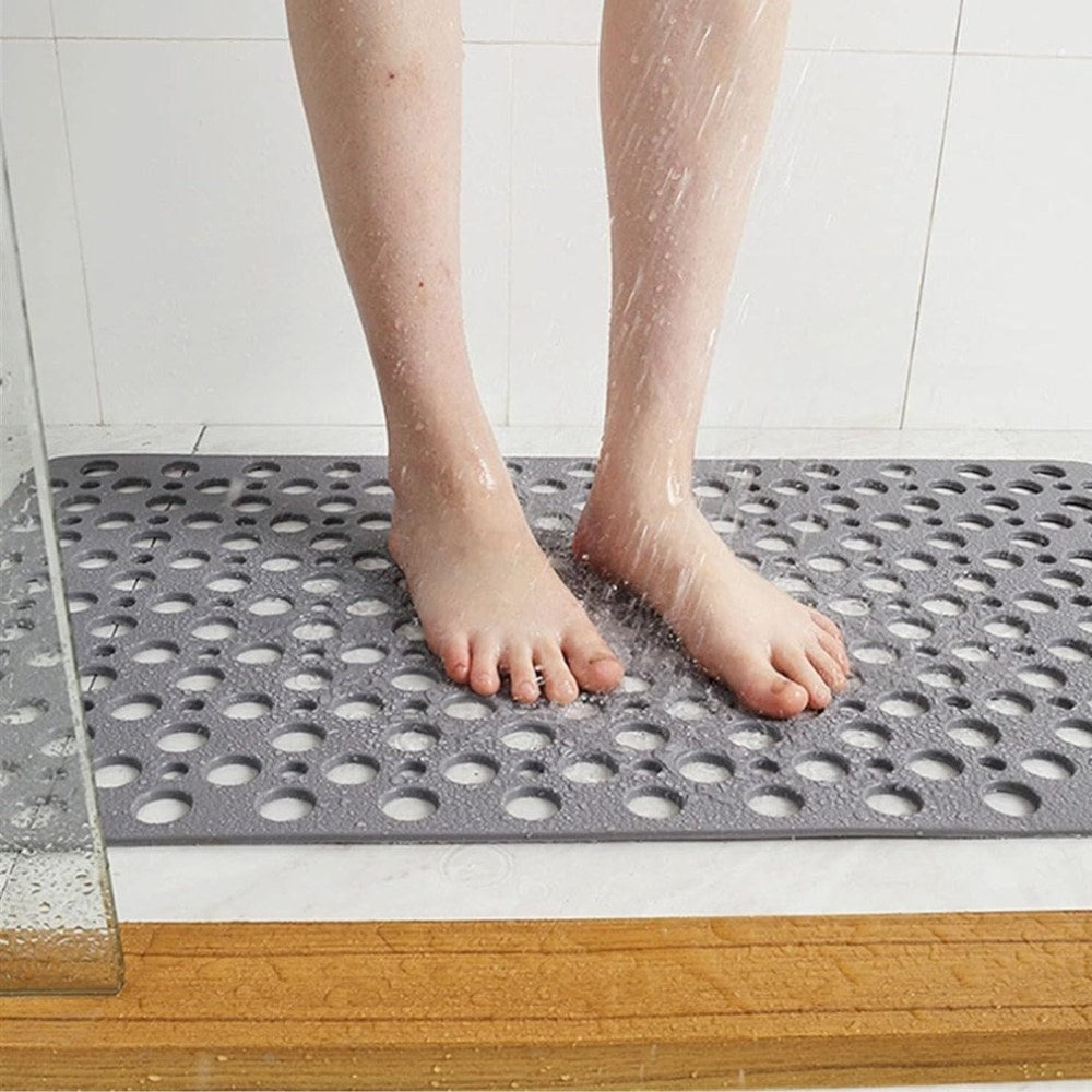 Bare feet standing on a gray shower mat under running water