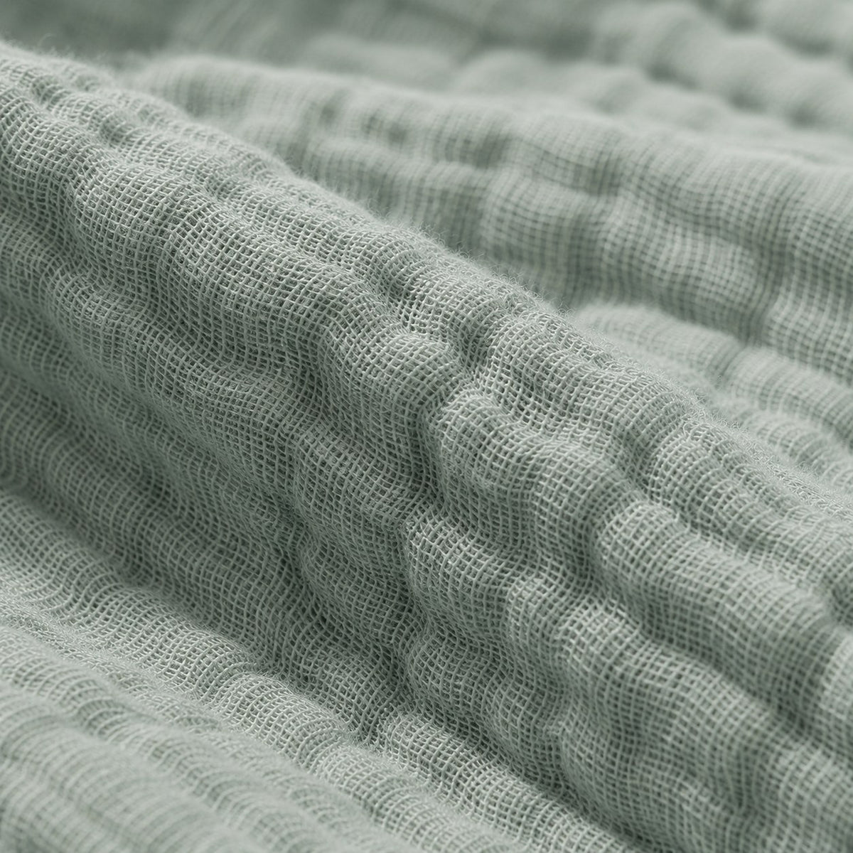 Close-up of the sage cotton muslin, showing the individual threads of the open plain weave, the small square gaps between them and the soft puckering where the six layers are bonded
