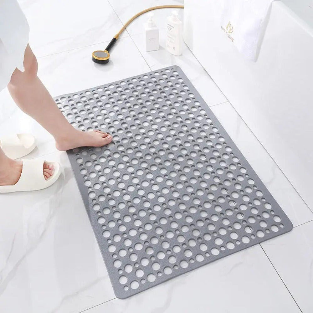A gray shower mat on a white marble bathroom floor, a bare foot stepping onto it