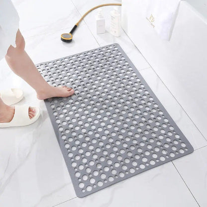 A gray shower mat on a white marble bathroom floor, a bare foot stepping onto it