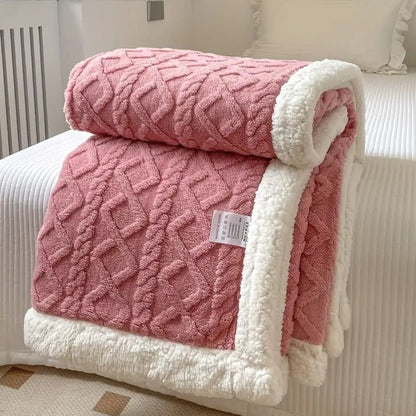 Pink sherpa throw blanket folded on a bed, the raised cable texture facing out and the white sherpa lining showing at the fold