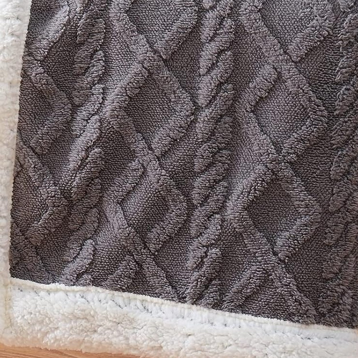 Close view of the cable and diamond texture raised out of the pile, above the bound sherpa edge