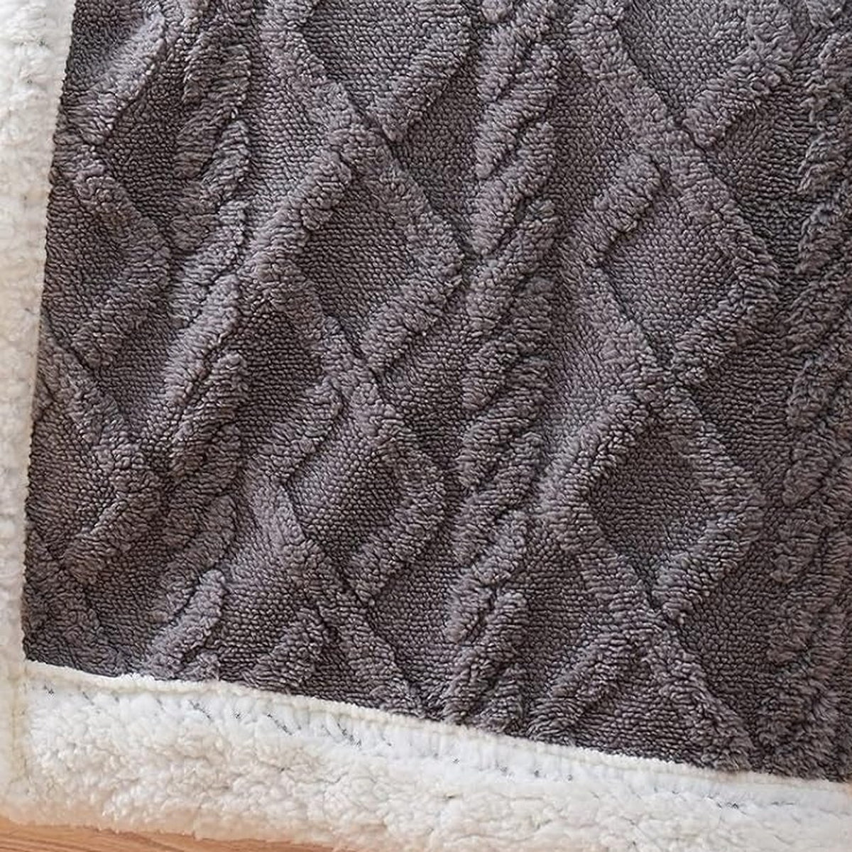 Close view of the cable and diamond texture raised out of the pile, above the bound sherpa edge
