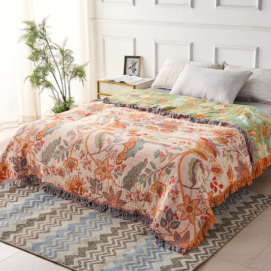 The floral cotton throw spread across a made double bed, cream face up, with a band of the sage green reverse folded back at the head and the tassel fringe hanging over the foot.