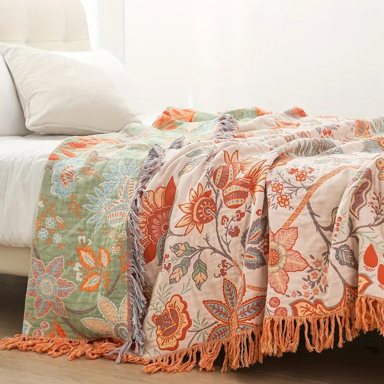 The foot of a bed with the throw laid over it, the knotted tassel fringe hanging toward the floor and the sage green face showing where the cloth folds back.