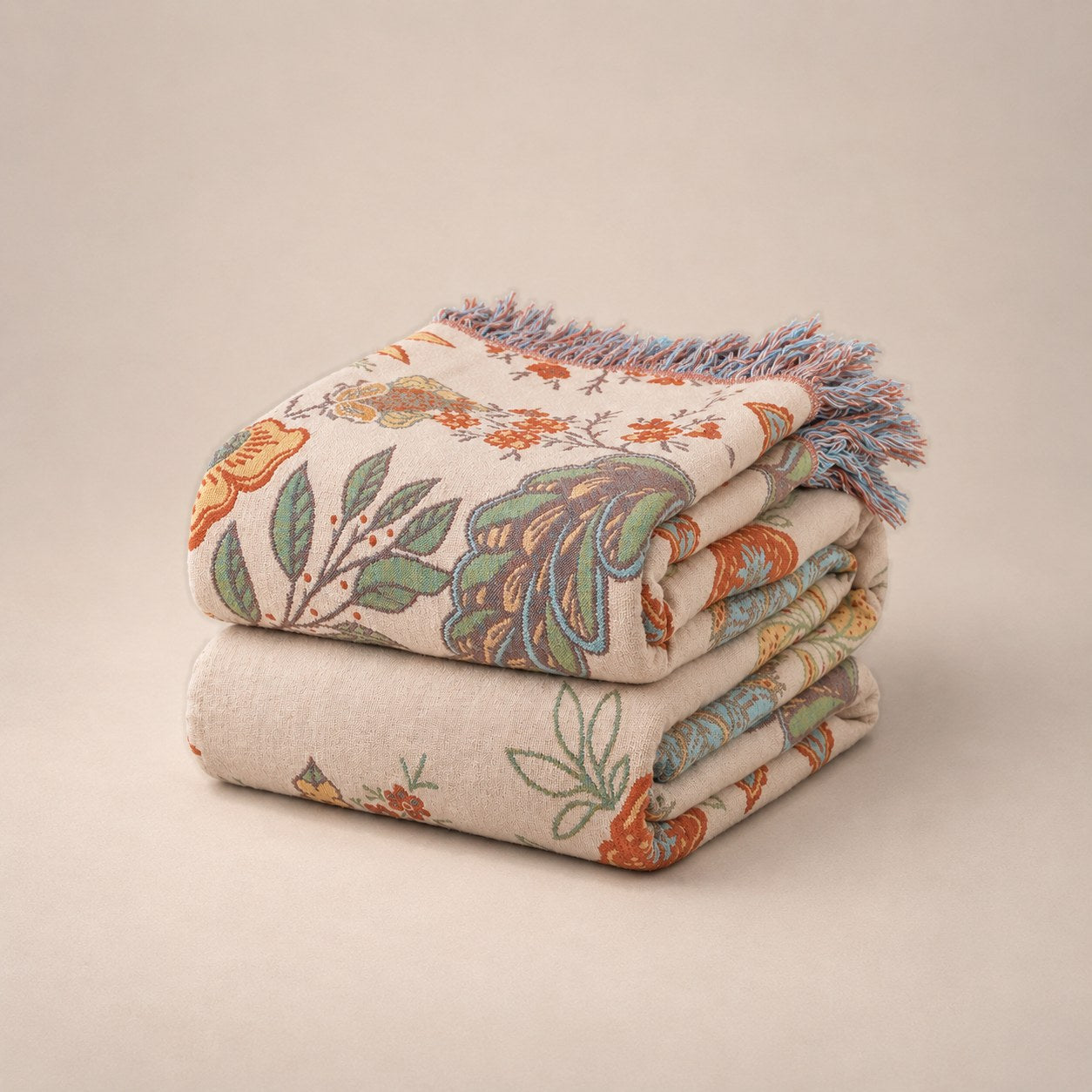 The floral cotton throw folded into a stack on a plain plaster background, the tassel fringe over the front edge.