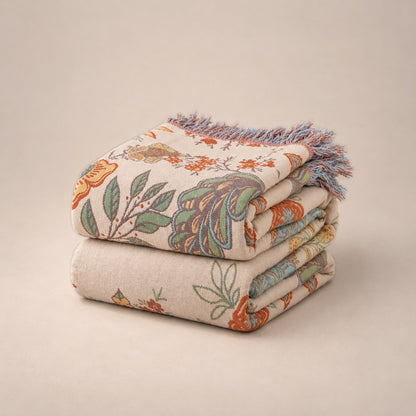 The floral cotton throw folded into a stack on a plain plaster background, the tassel fringe over the front edge.