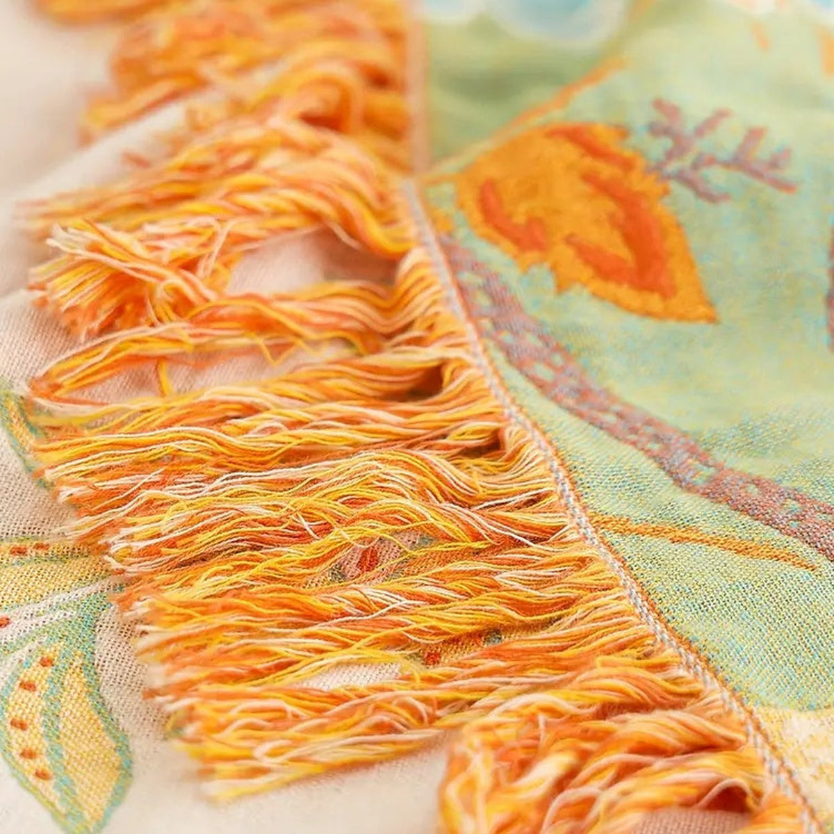 A close photograph of the knotted tassel fringe where it meets the woven edge, with the cream face on one side and the sage green face on the other.