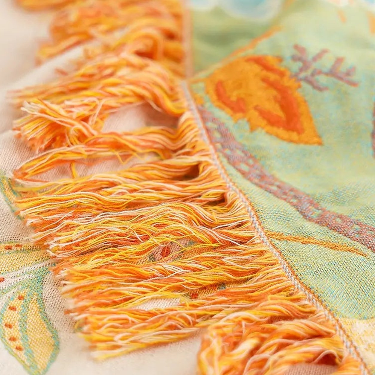 A close photograph of the knotted tassel fringe where it meets the woven edge, with the cream face on one side and the sage green face on the other.
